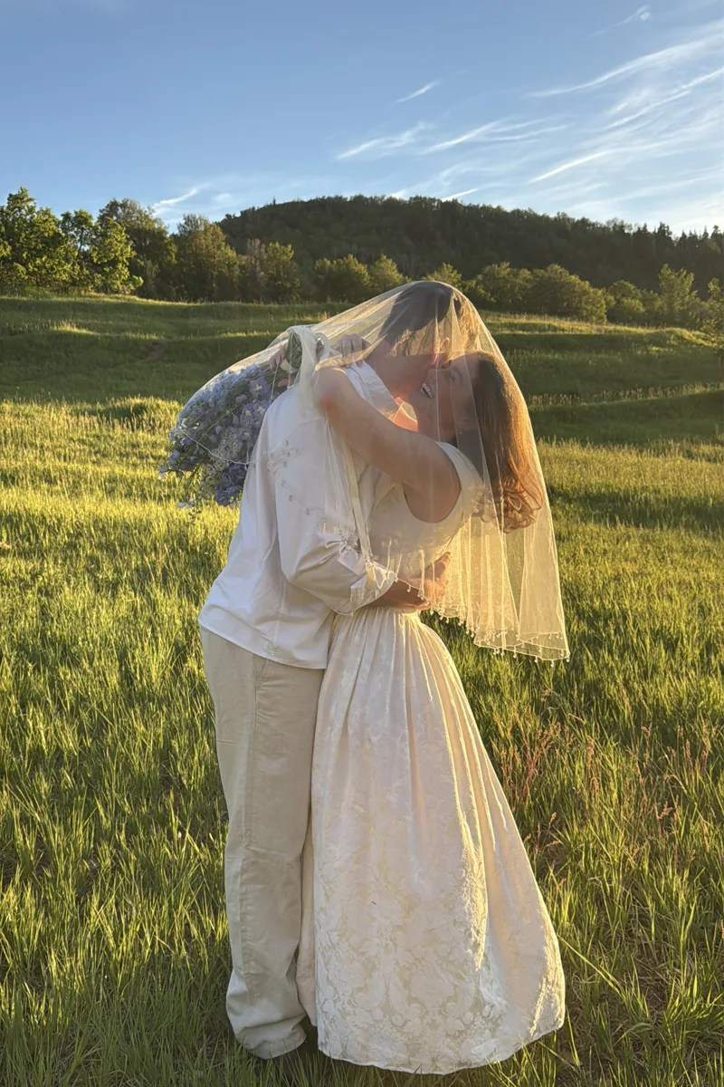 Couple kissing under a veil in a mountain meadow.