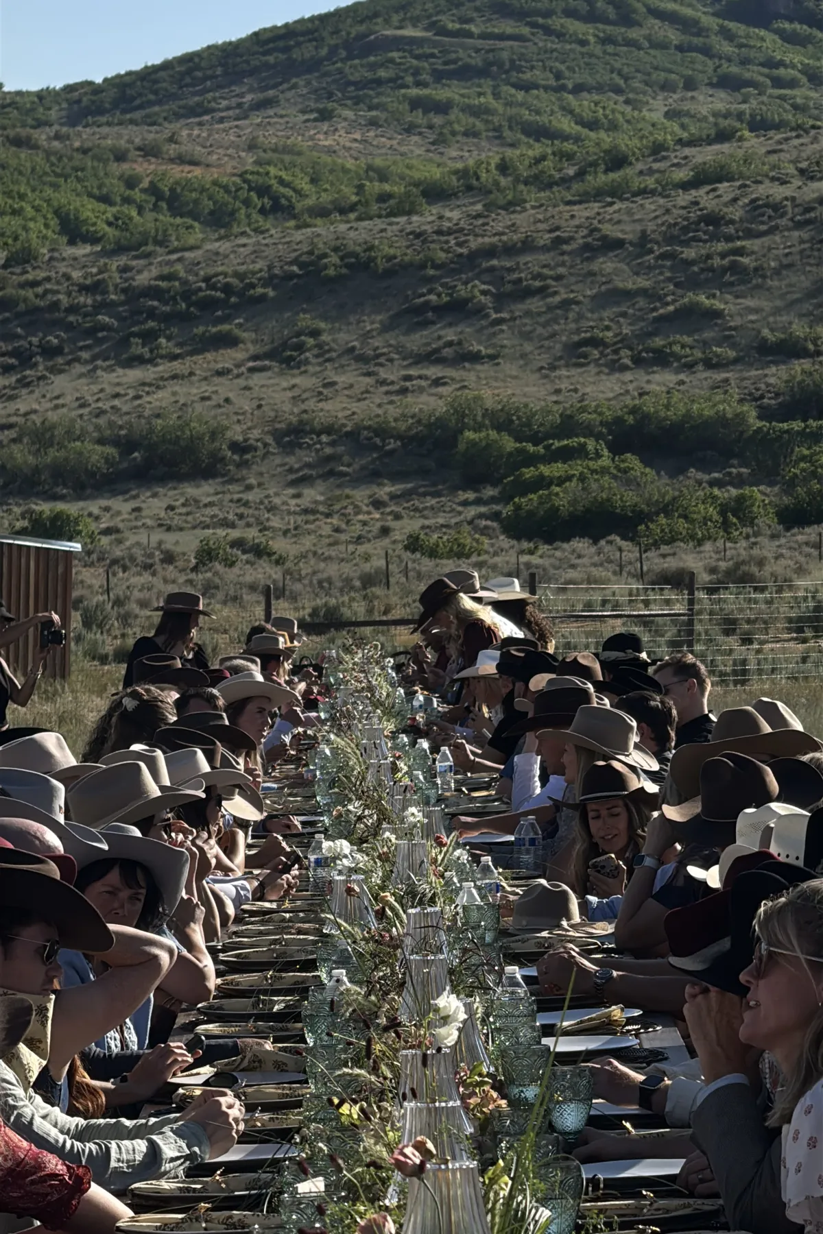 Guests in cowboy hats gathered at a long outdoor wedding table.