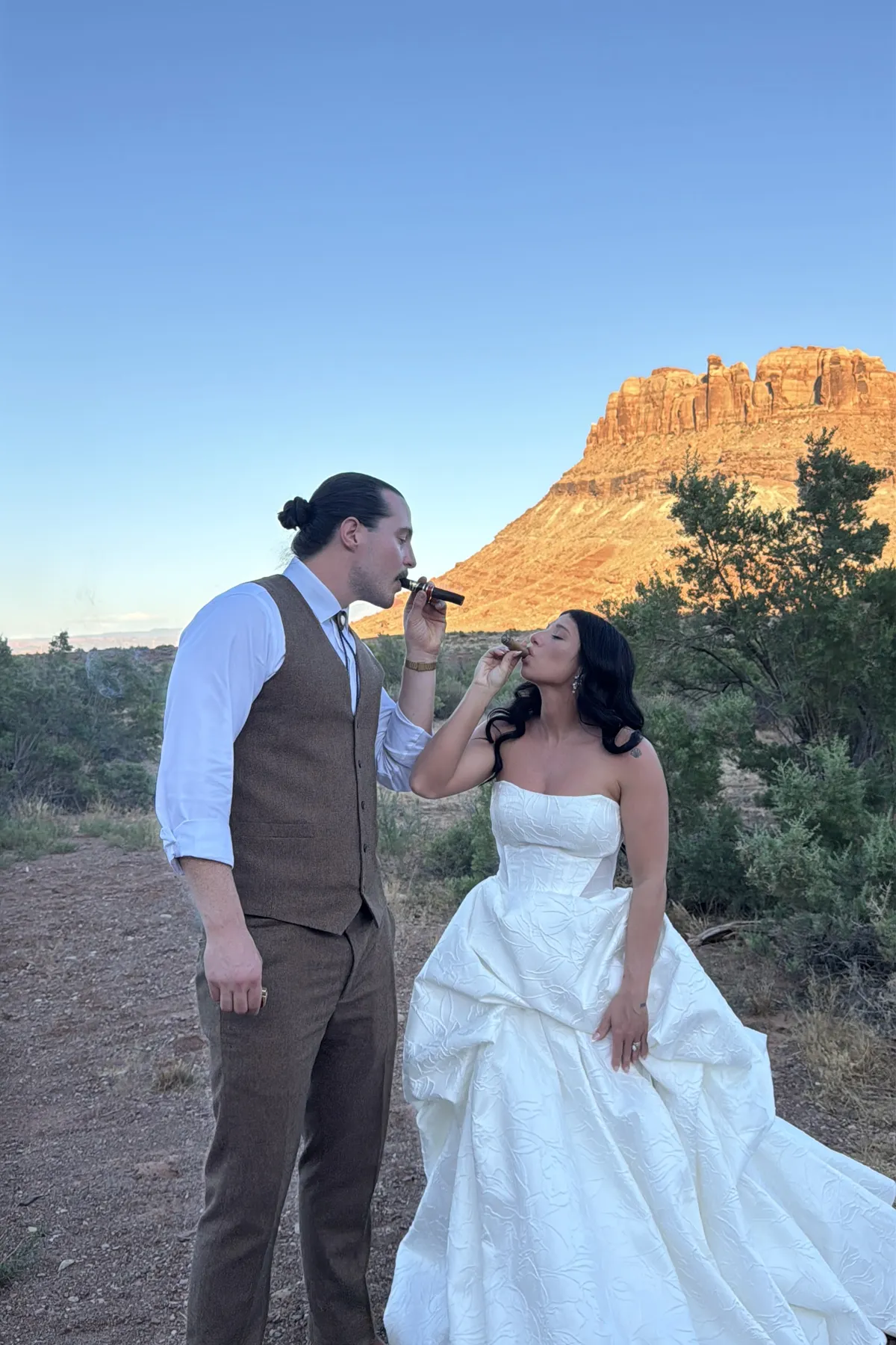 Bride and groom sharing a cigar at golden hour in the red rocks.