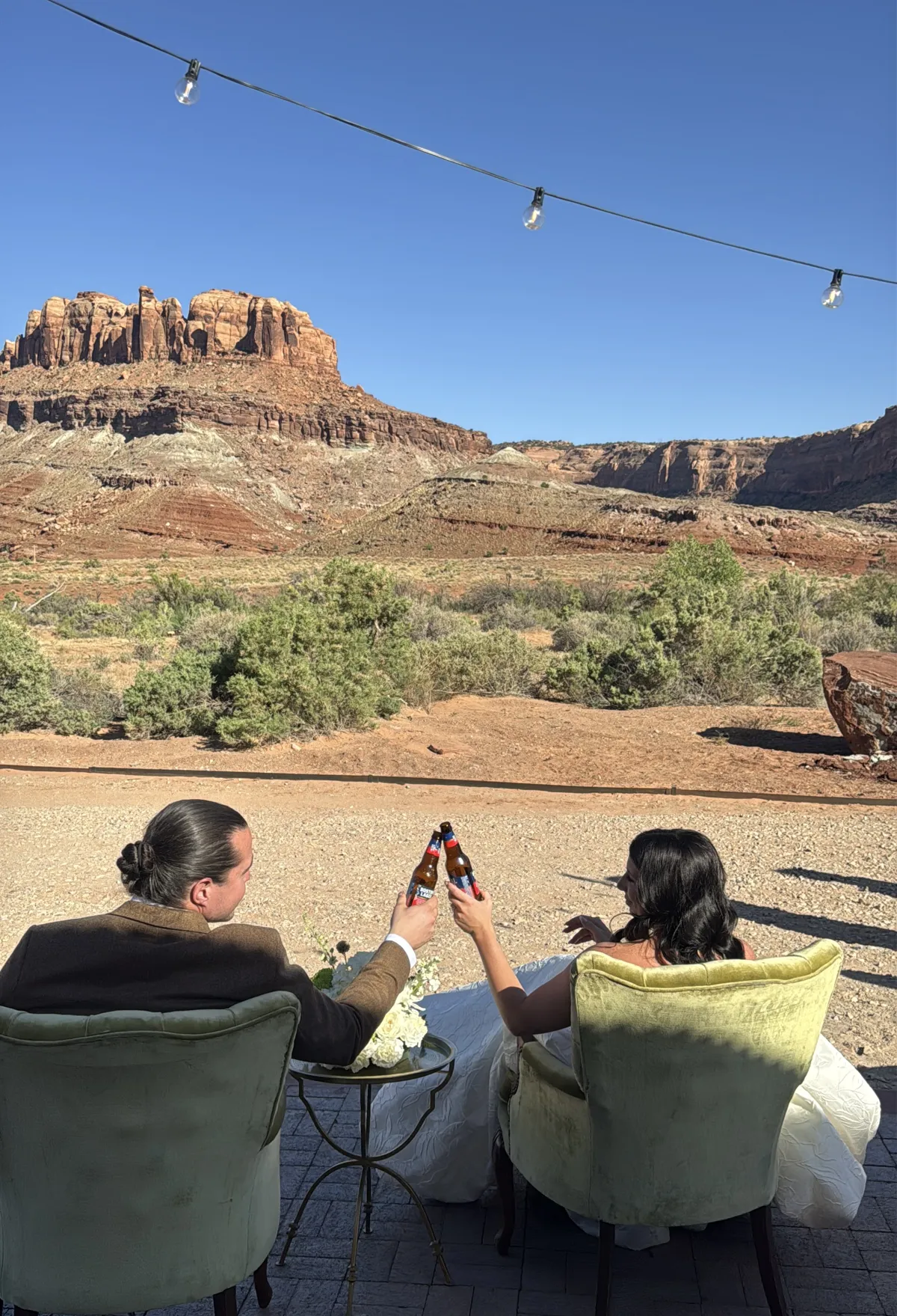 Couple toasting in vintage chairs beneath red rock cliffs.