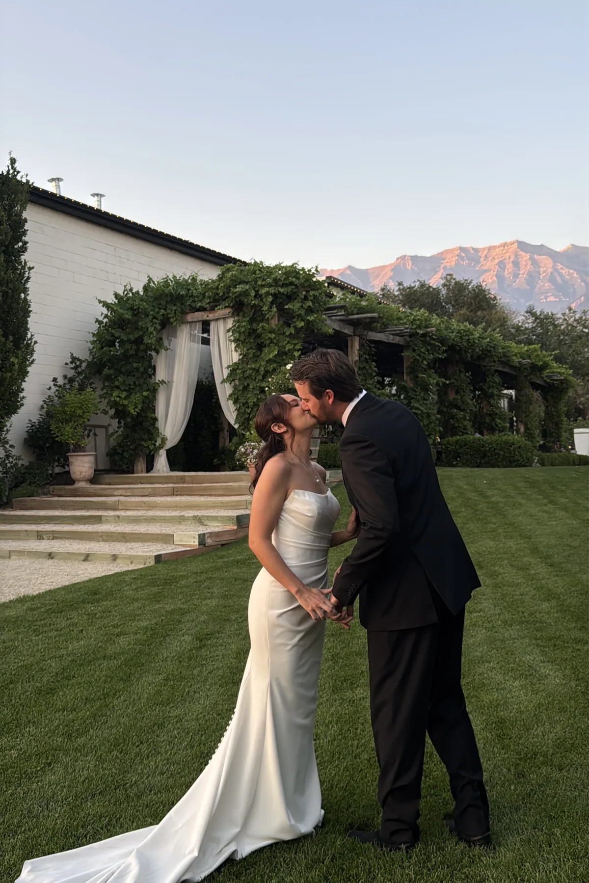 Couple kissing at a garden venue with mountains glowing behind them.