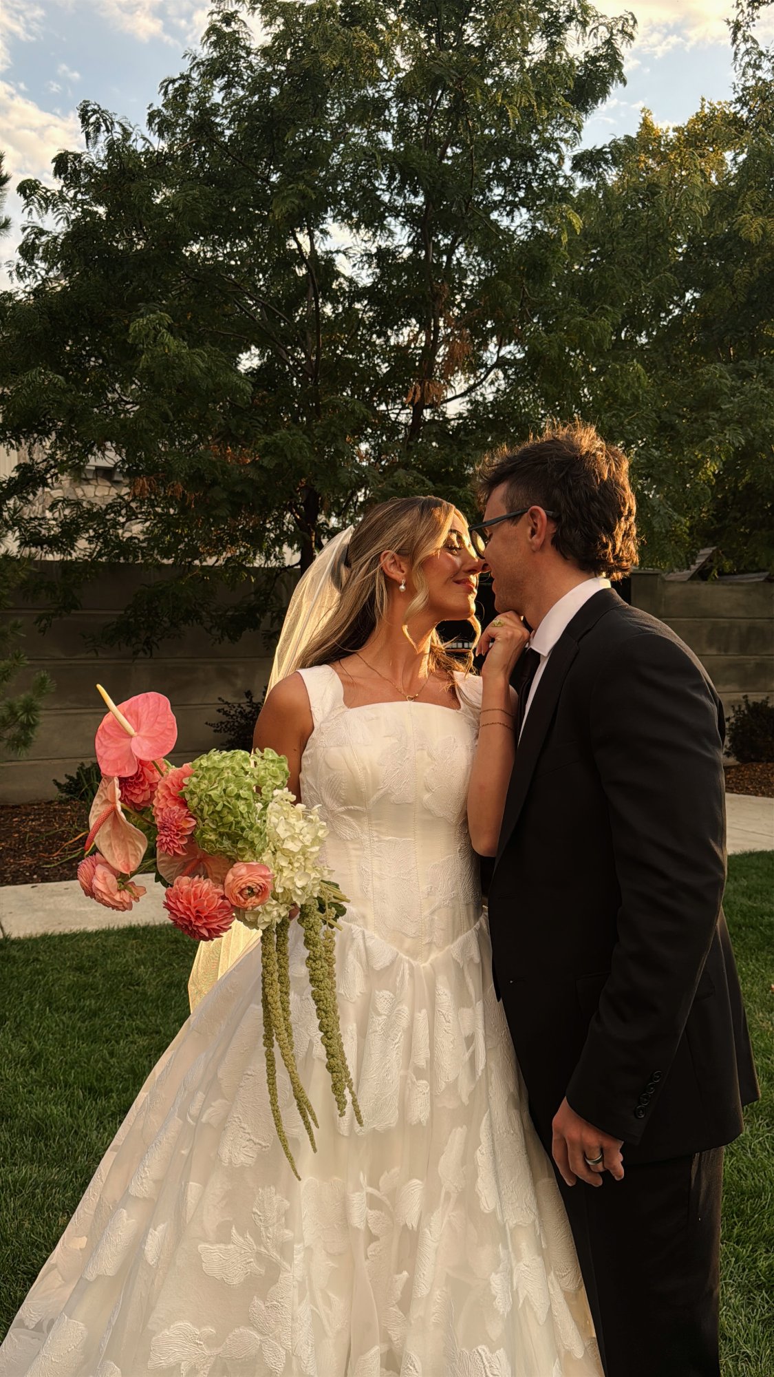 A bride and groom embracing outdoors, bride holding a bouquet